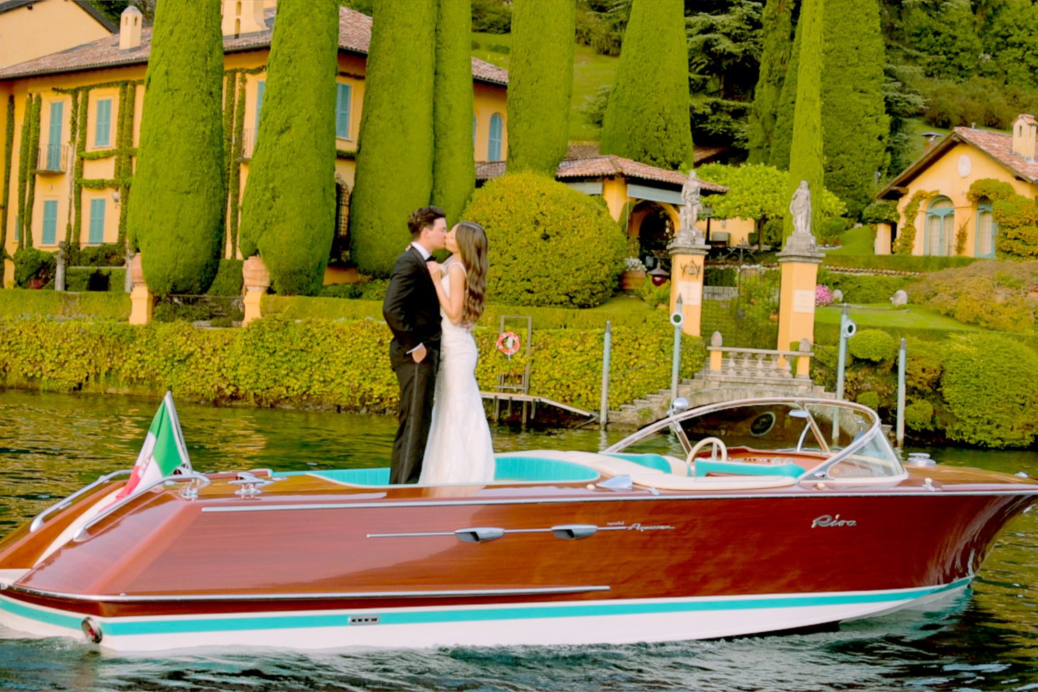 Bride and groom on a wooden boat gliding across Lake Como near Villa Balbiano — captured by Koman Studio, fine-art wedding photographers and filmmakers in Italy.