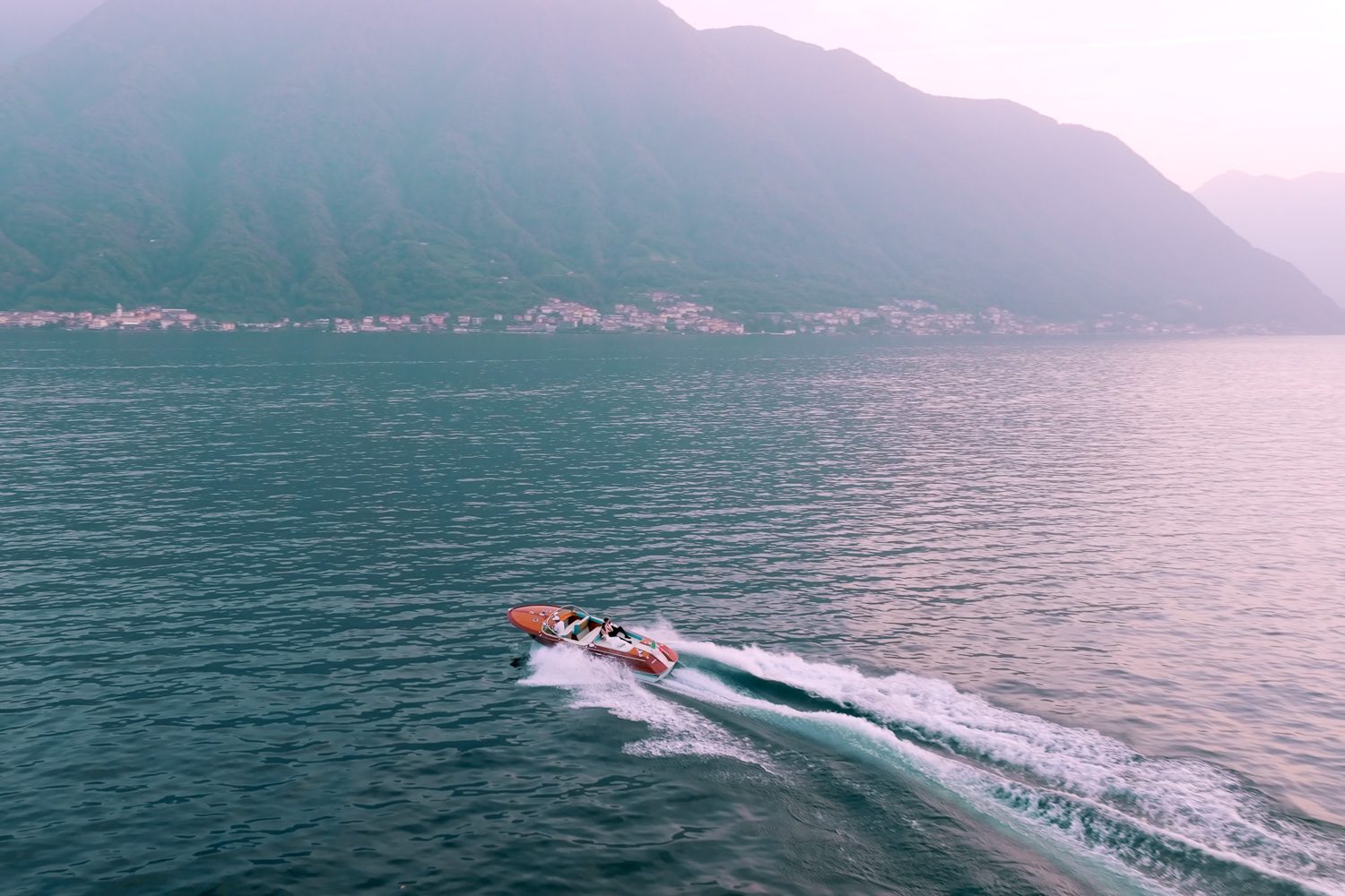 Aerial drone shot of the bride and groom on a wooden boat gliding across Lake Como near Villa Balbiano — captured by Koman Studio, fine-art wedding photographers in Italy.
